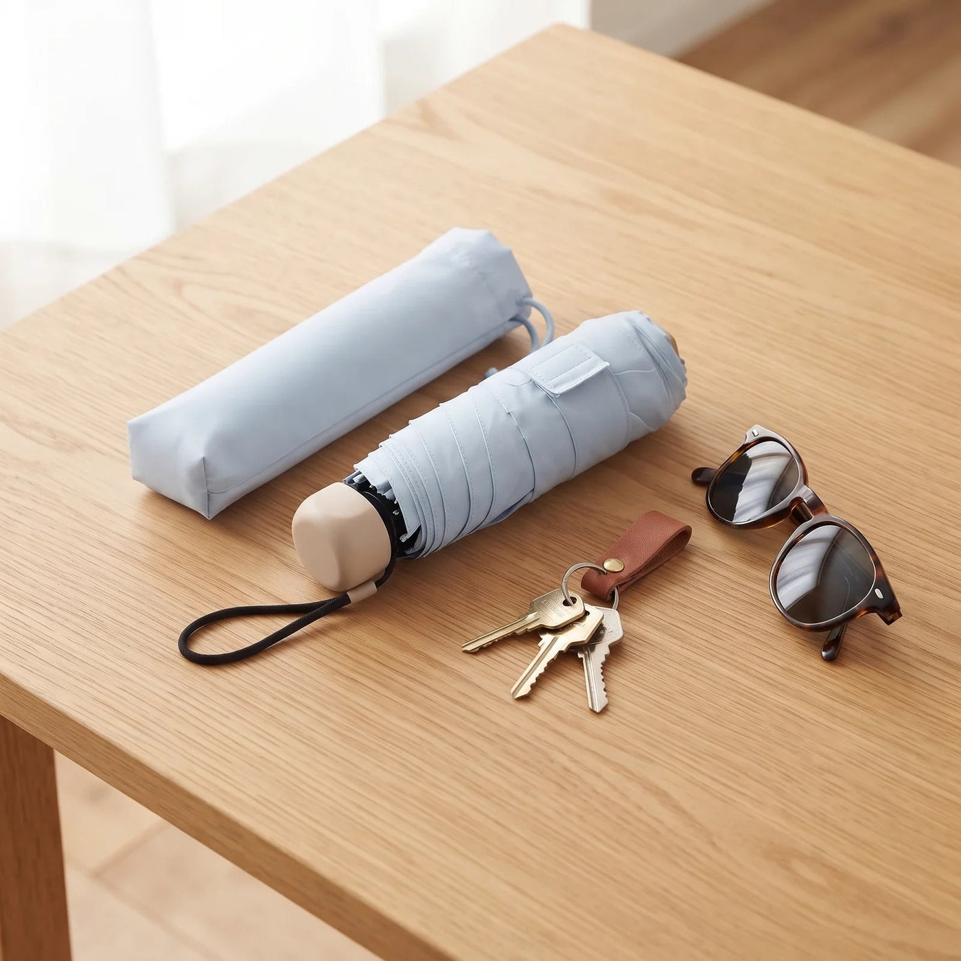 Umbrellys pocket umbrella folded on a table with its sleeve, keys and sunglasses
